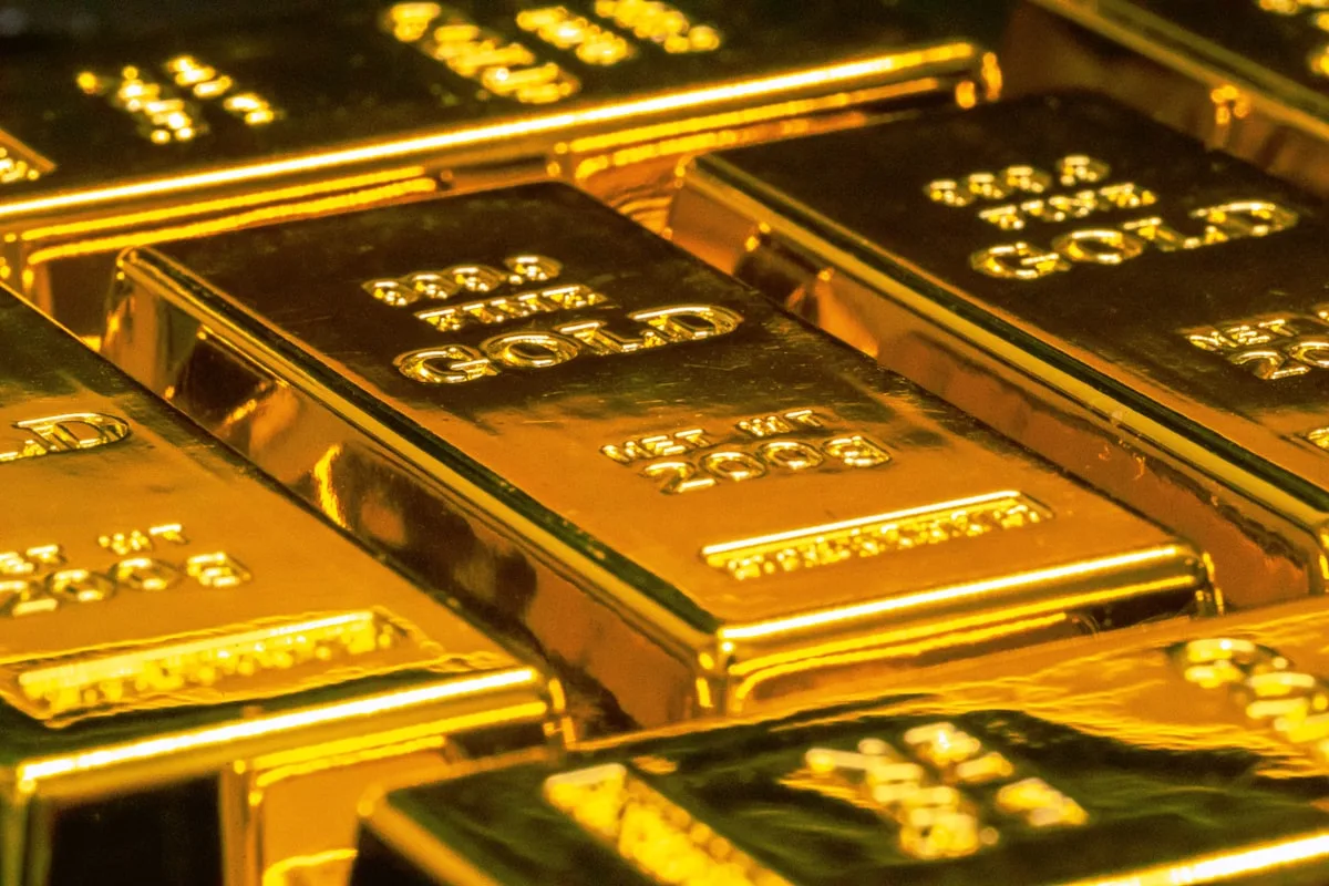 Stacked gold bars under directional light, with a slight reflective sheen — illustrative imagery for Newsorga's coverage of Monday, May 11, 2026 commodity moves in which spot gold fell 1% to $4,669.82/oz and Brent crude rose 4.11% to $105.45/bbl after US President Donald Trump rejected Iran's 14-point peace proposal as 'totally unacceptable' on Truth Social on Sunday afternoon.