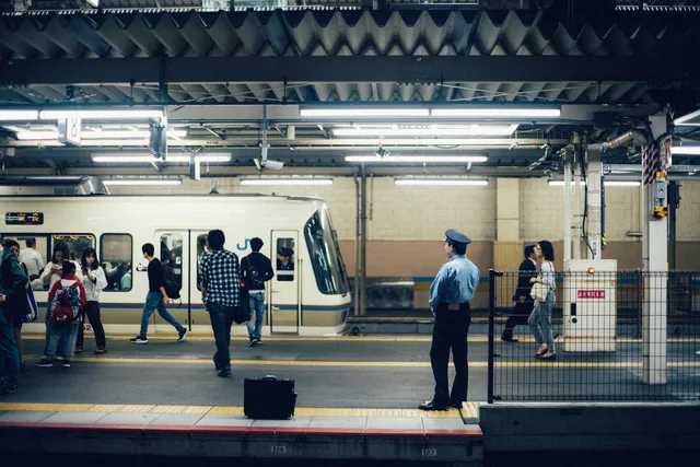 Commuters standing on a Japanese rail platform beside a white commuter train at dusk — illustrative imagery for the JR East Tokaido Line train that was halted at Kawasaki Station in Kanagawa Prefecture on the afternoon of May 10, 2026 after passengers reported an unknown substance was sprayed inside one of the carriages