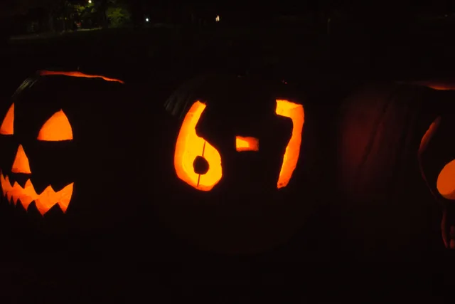 Nighttime photo in Toronto of lit jack-o'-lanterns and people in costume holding open palms in the viral "six-seven" hand gesture (Wikimedia Commons).